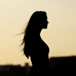 A woman with long hair standing at dusk.